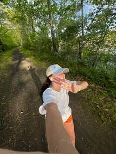 a woman is taking a selfie while walking down a path in the woods with trees