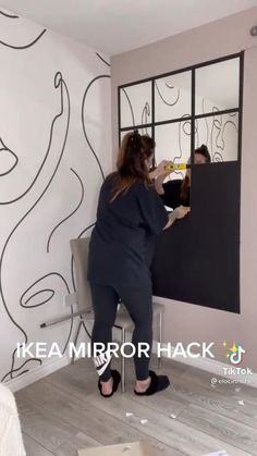 a woman standing in front of a mirror with her reflection on the wall behind her