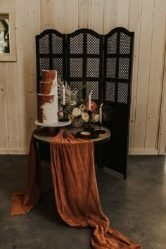 a table topped with a cake next to a black chair and wooden paneled wall