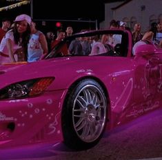 a pink sports car parked in front of a crowd