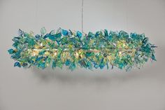 a long glass chandelier hanging from the ceiling with blue and green leaves on it