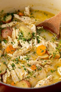 a pot filled with chicken, potatoes and carrots next to a wooden ladle