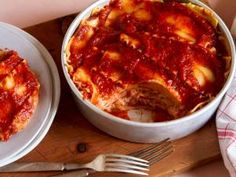 two white plates topped with lasagna next to a fork and knife on a cutting board