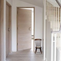 a wooden chair sitting in the middle of a hallway next to a white wall and stairs