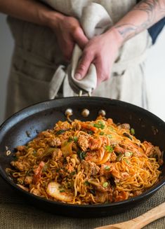 a person holding a fork in a skillet with noodles and meats on it