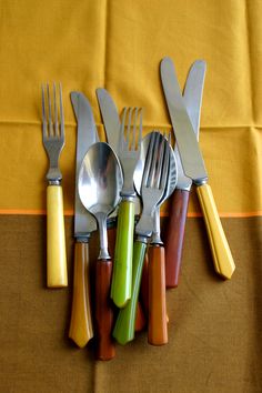 forks, knives and spoons are lined up on a yellow tablecloth with an orange border