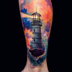 a man's leg with a watercolor lighthouse tattoo on his left side and an ocean wave coming towards him