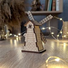 a small wooden windmill sitting on top of a table next to some string lights and a tree