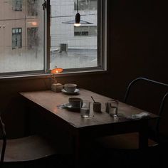 a table and chairs in front of a window with rain coming down on the street