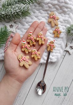 hand holding spoon with decorated sugar cookies on white wooden table next to christmas tree and snowflakes