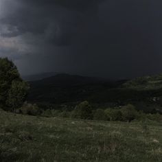 a black and white photo of a storm moving through the sky over a grassy field