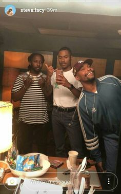 three men standing in front of a table with food and drinks on top of it