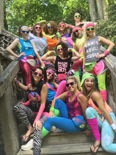 a group of women in colorful clothing posing for a photo on a wooden bridge with trees behind them