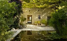 an outdoor area with water, plants and chairs in the middle of it is surrounded by greenery