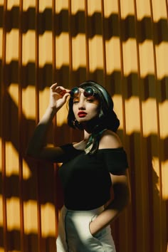 a woman in black shirt and white pants standing next to a wall with shadows on it