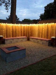 an outdoor fire pit surrounded by wooden fence with string lights on the top and bottom