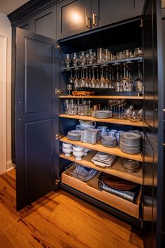 an open cabinet with dishes and glasses on the bottom shelf, in a room that has hardwood floors