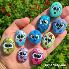 five painted rocks in the shape of cartoon faces are held by someone's hand