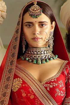 a woman in a red sari with jewelry on her neck and headpieces