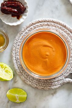 an orange sauce in a glass bowl surrounded by limes and other condiments