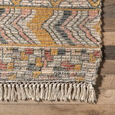 a multicolored rug with tassels and fringe on a wooden floor