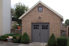 a brick building with two garages on each side and bushes in the front yard