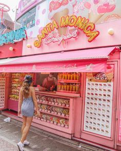 a woman standing in front of a pink store with lots of food on display outside