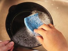 a person is cleaning a sink with a blue sponge on the bottom and a hand holding a rag over it