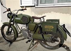 an old green motorcycle parked next to a building