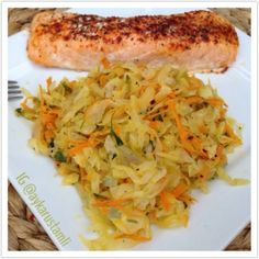 a white plate topped with coleslaw next to a piece of salmon on top of a table