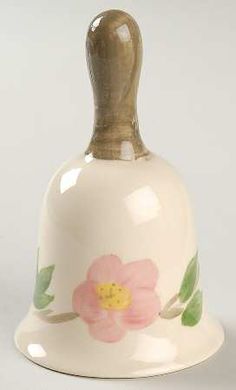 a white bell with a flower painted on it's side and a wooden handle