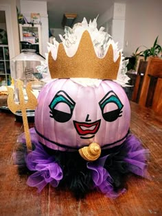 a purple pumpkin with a crown on it's head sitting on a wooden table