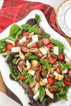 a salad with strawberries and pecans in it on a white platter next to a red napkin