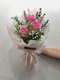 a bouquet of pink roses wrapped in white paper with greenery and baby's breath