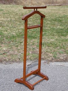 a wooden coat rack sitting on the side of a road next to a grass covered field