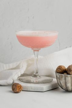 a pink drink in a glass next to nuts on a white tablecloth and napkin