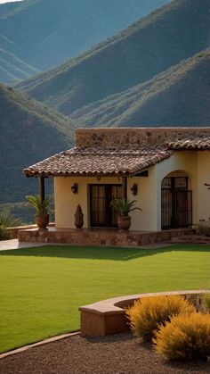 a house with mountains in the background and green grass on the front lawn, surrounded by shrubs