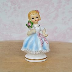 "This vintage figurine is lovely! Made of ceramic, it features a blonde girl holding a flower bouquet, there are flowers on her skirt and in her hair, there's spaghetti trim along the front of the skirt, and gold-painted accents.  Measures just under 2.75\" long x 2.15\" wide x 4.5\" high.  Maker : Made in Japan.  Time Period : 1950's. Condition : Good.. There is crazing throughout the entirety of the figurine, light paint wear, light wear on the spaghetti trim, and light dirt wear on the 'skin. Holding A Flower, Dog Brooch, Vintage Headbands, Ceramic Figurine, Vintage Souvenir, Vintage Dog, Ceramic Figurines, Light Painting, Blonde Girl