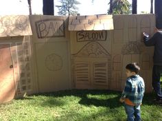 a young boy standing in front of a cardboard wall with drawings on it and another man writing