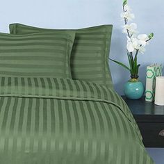 a bed with green and white striped comforter next to a blue vase filled with flowers