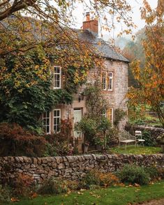 an old stone house surrounded by trees and flowers in the fall with leaves on the ground