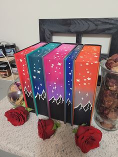 four boxes with different designs on them sitting on a table next to some red roses