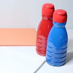 two red and blue water bottles sitting next to each other on a white counter top