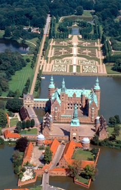 an aerial view of a castle with orange roofs and water in the foreground, surrounded by lush green trees