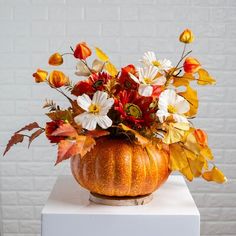 a pumpkin shaped vase filled with flowers on top of a white table next to a brick wall