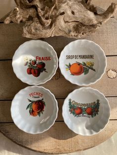 four plates with fruit painted on them sitting on top of a wooden table next to driftwood