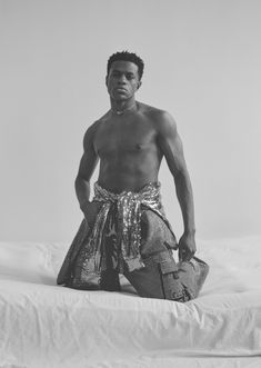 a shirtless man sitting on top of a bed with his hands in his pockets