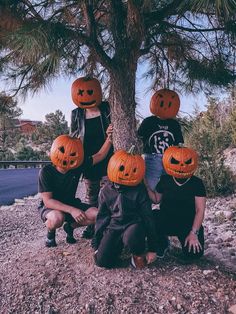 four children wearing pumpkin heads sitting under a tree