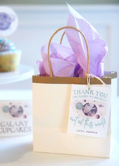 there is a bag with some purple tissue paper on it and a cupcake in the background