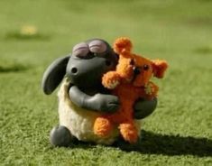 two stuffed animals sitting in the grass with one being held up by another animal's leg